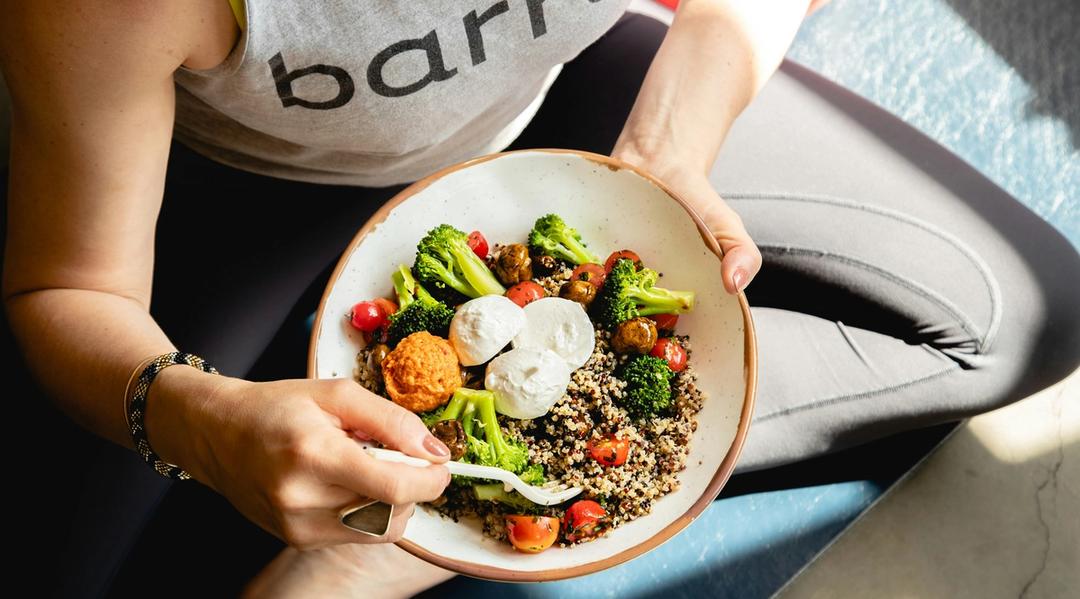 A woman holding a meal with vegetables and quinoa
