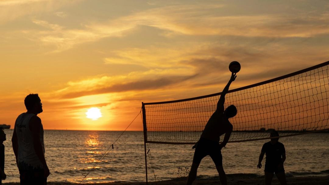 People playing beach volleyball at sunset by the ocean.
