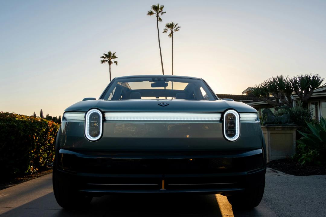 Front view of a modern Rivian electric vehicle showcasing its distinctive LED light bar and signature oval headlights at sunset.