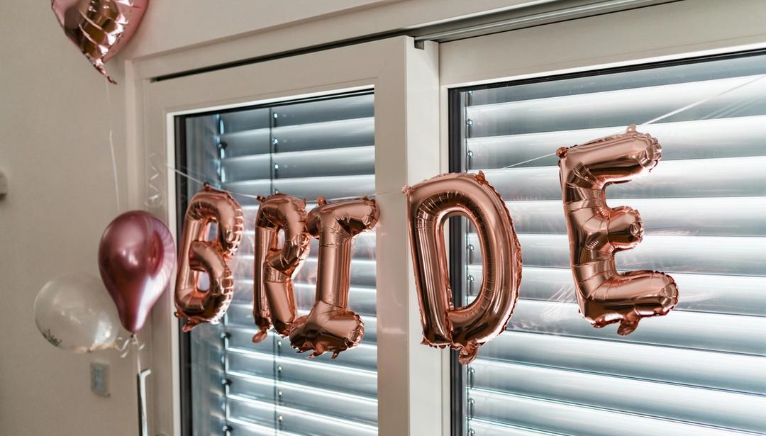 A pink balloon banner that reads "bride", hanging from a window.
