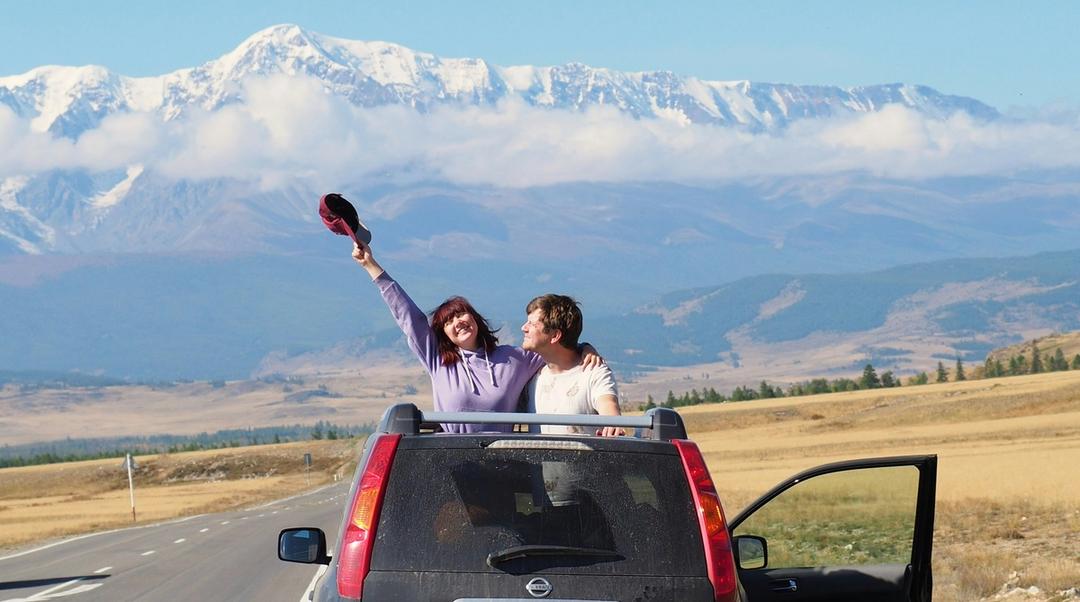 A couple standing on top of a car with a mountain scenery.