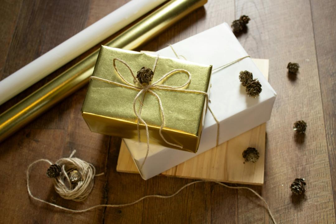 Two gifts wrapped and stacked next to wrapping paper, twine, and pine cones.