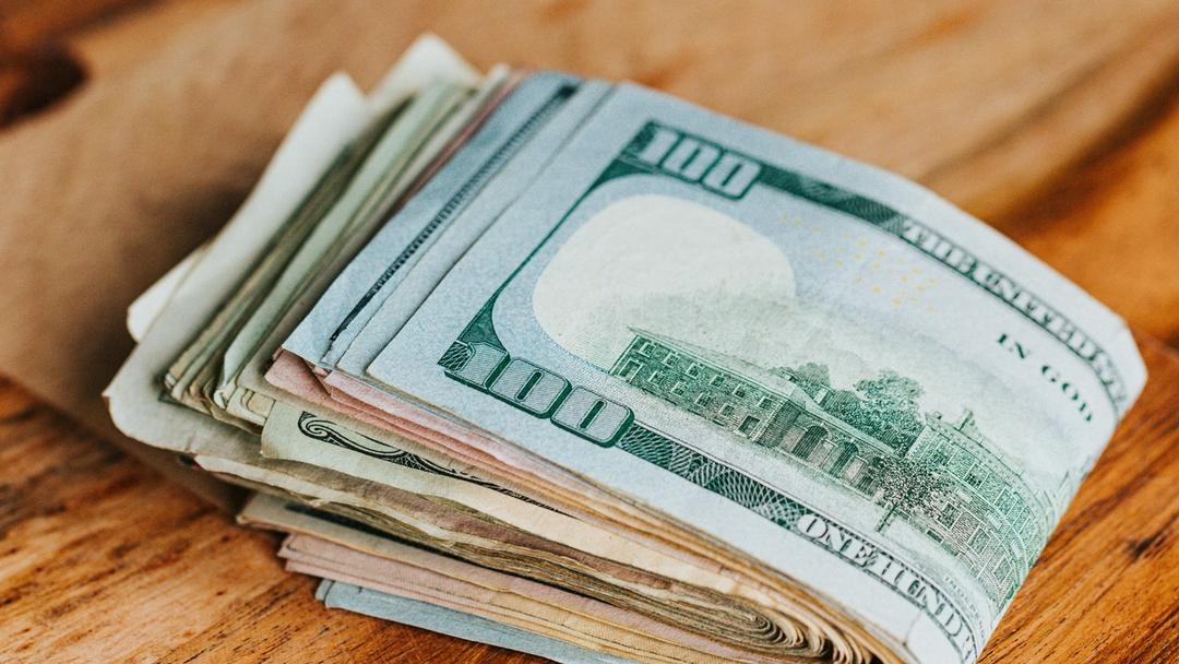 A wad of cash sitting on a wooden table.