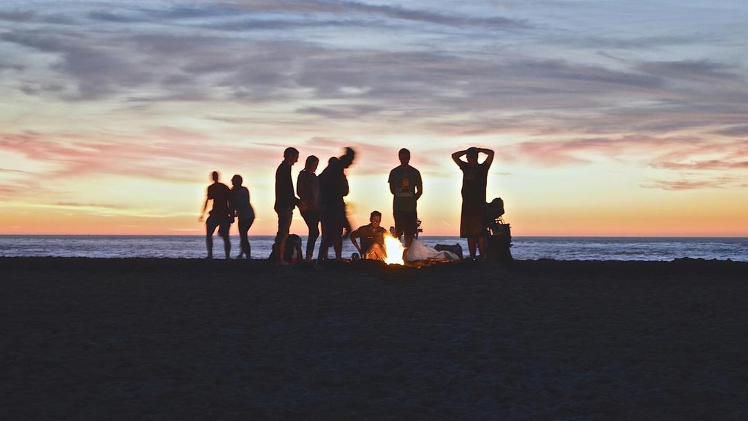 Group of people watching the sunset with a campfire.