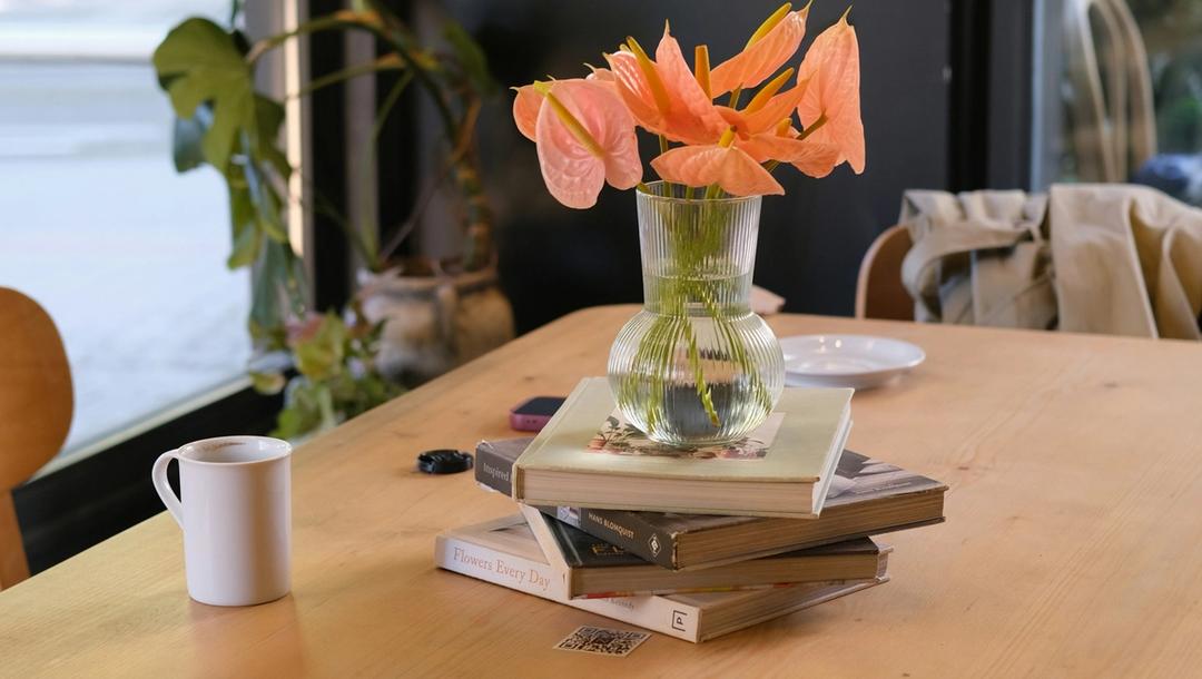 A vase of orange flowers sitting on top of a pile of books on a table.