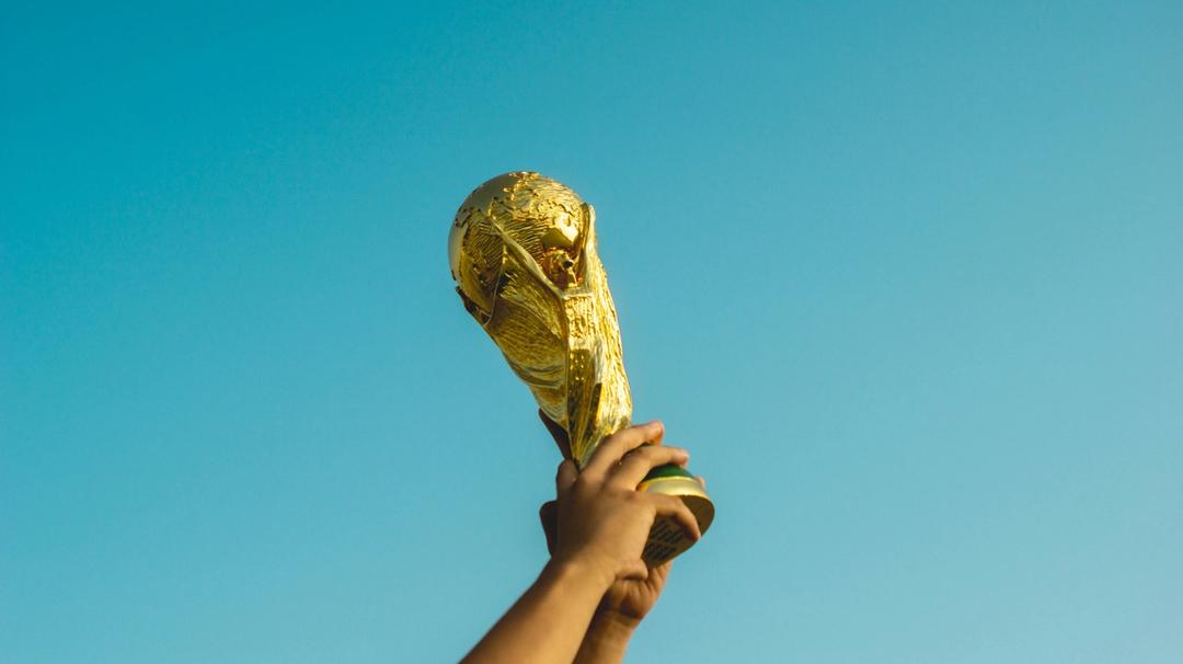 A person holding a gold world cup trophy in the air.