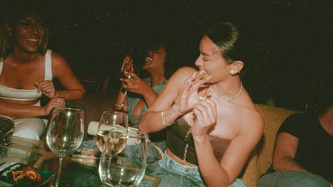 A group of women sitting around a table laughing, with wine glasses.