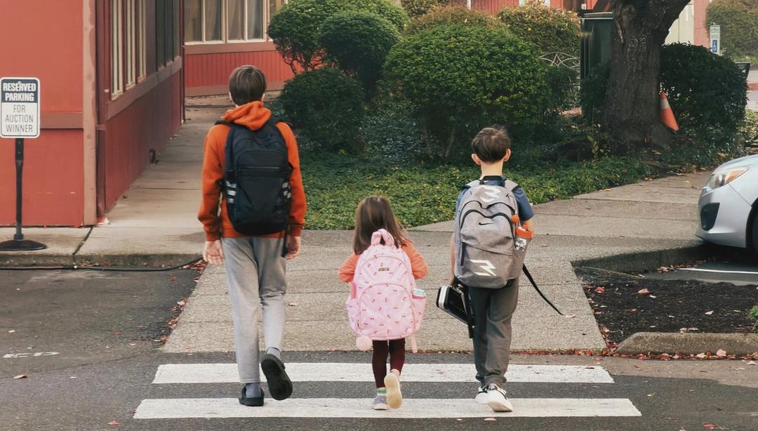 three children with backpacks crossing the street.