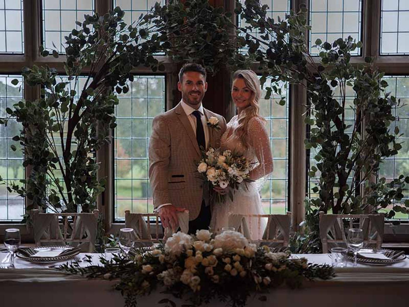 Bride and groom embracing under a floral arch by the leaded windows at Delta Hotels Breadsall Priory Country Club