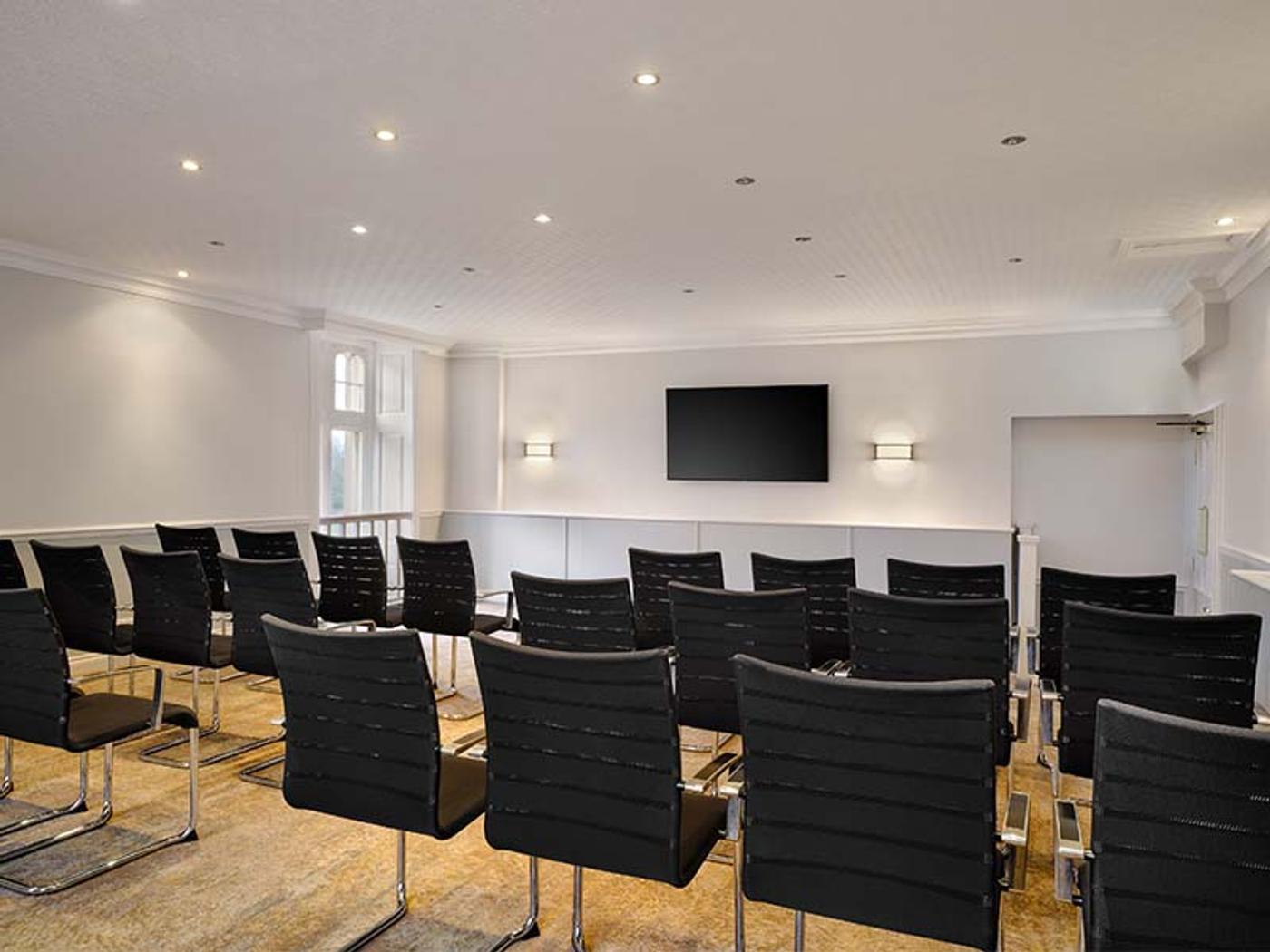 Meeting room set theatre-style with rows of chairs facing a wall-mounted screen