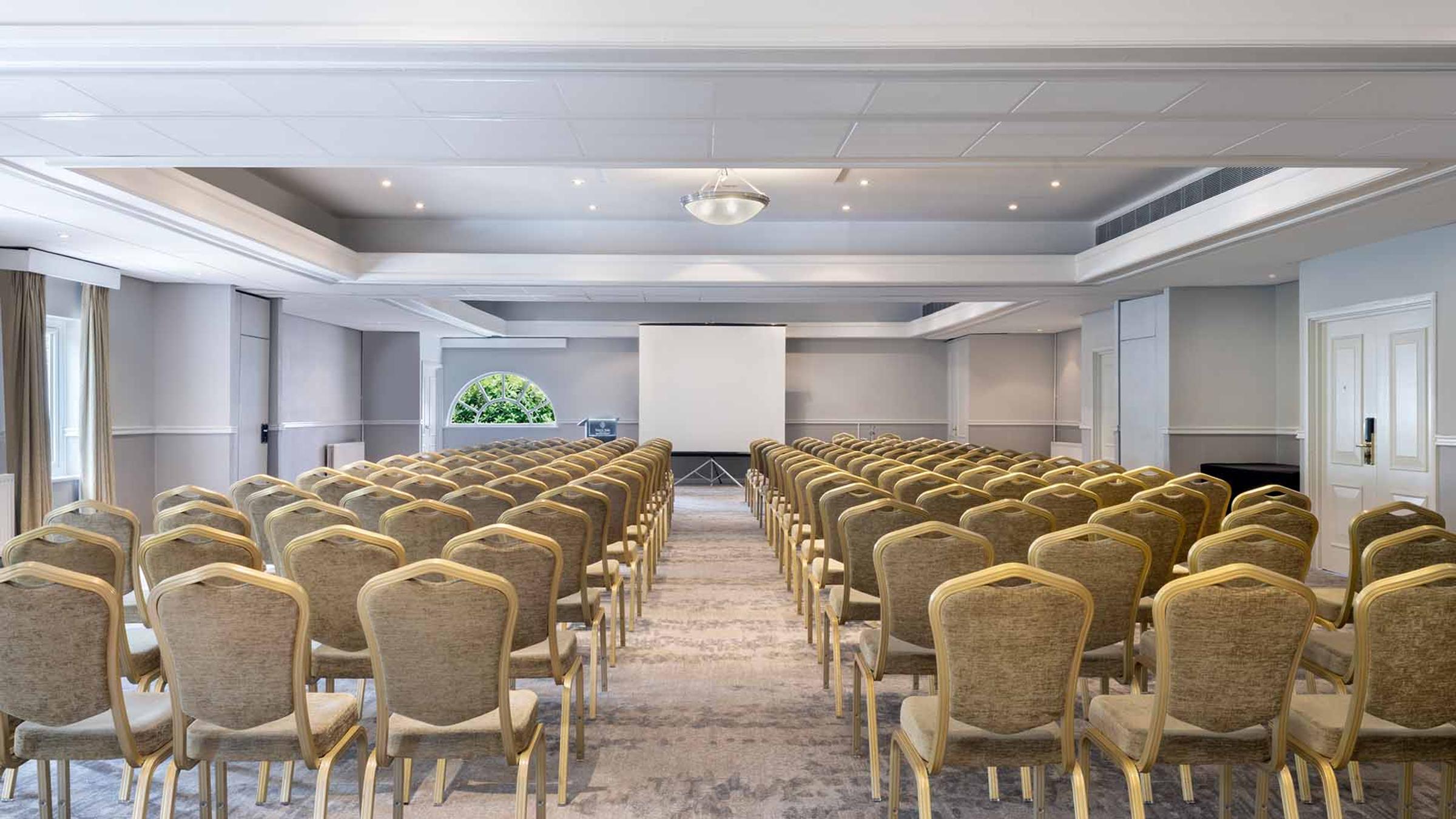 Conference room set theatre-style with rows of chairs facing a projector screen