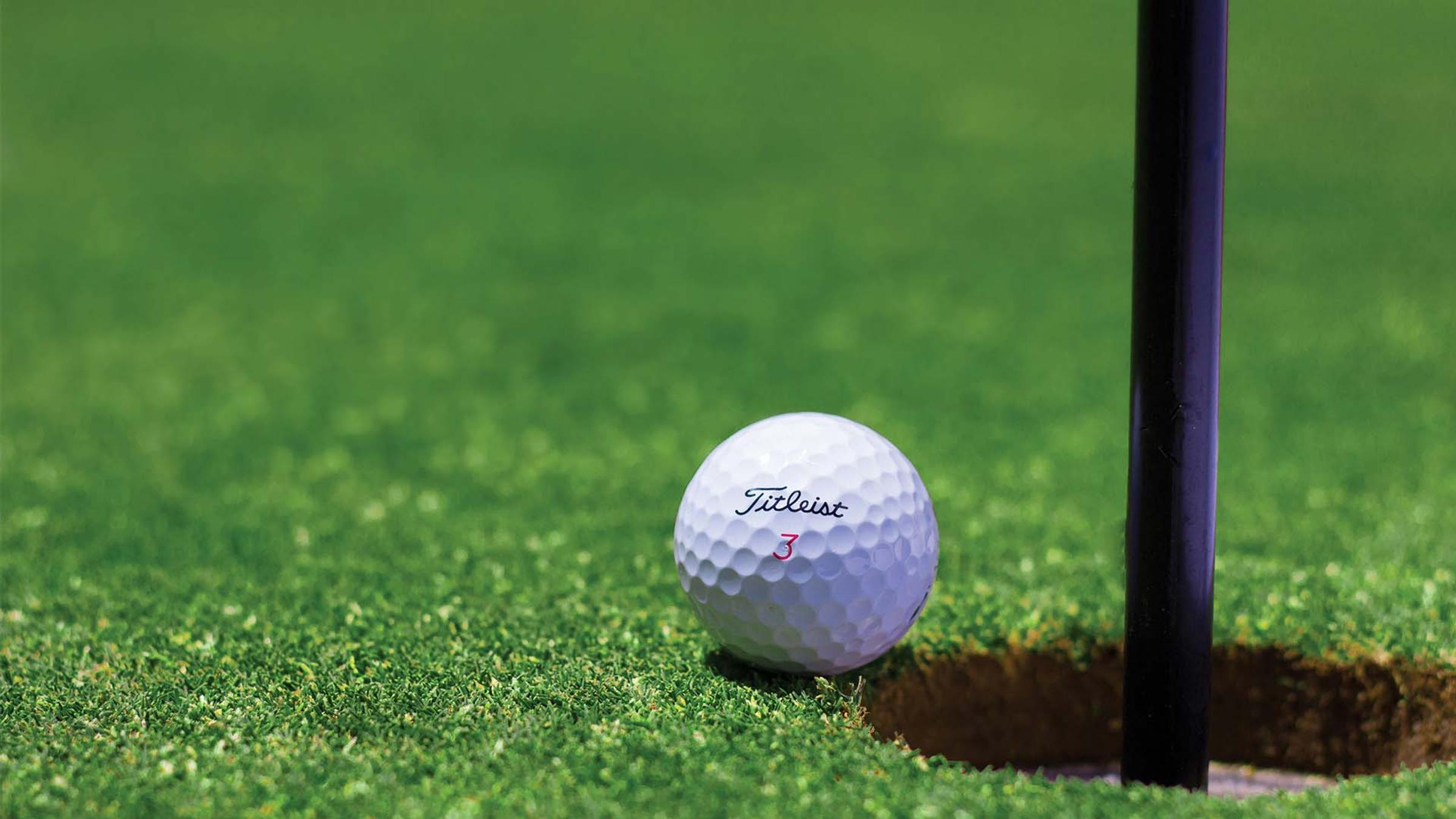 Golf ball resting on the lip of the hole beside the flagstick