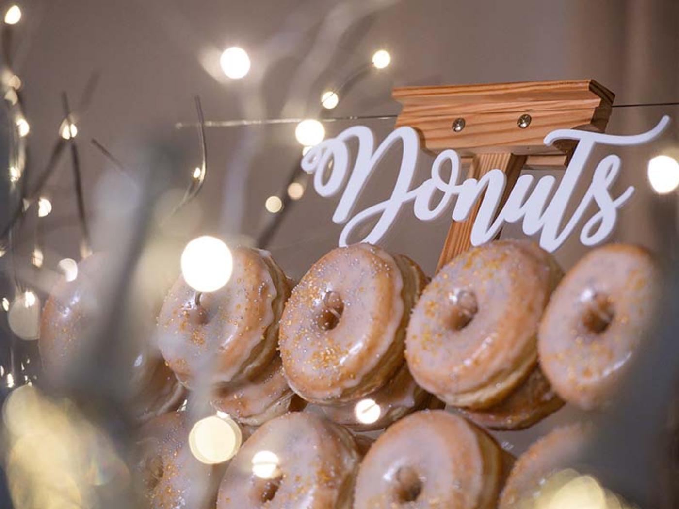 Wooden donut stand with a hand-lettered 'Donuts' sign and fairy lights