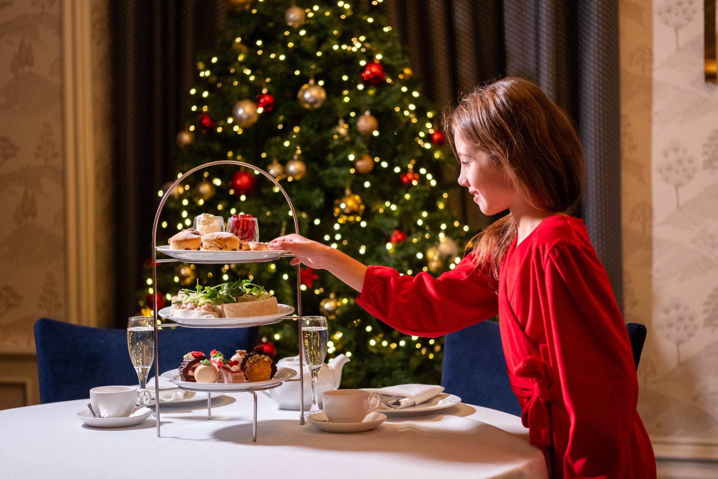 Girl taking cake from afternoon tea stand in front of Christmas tree.