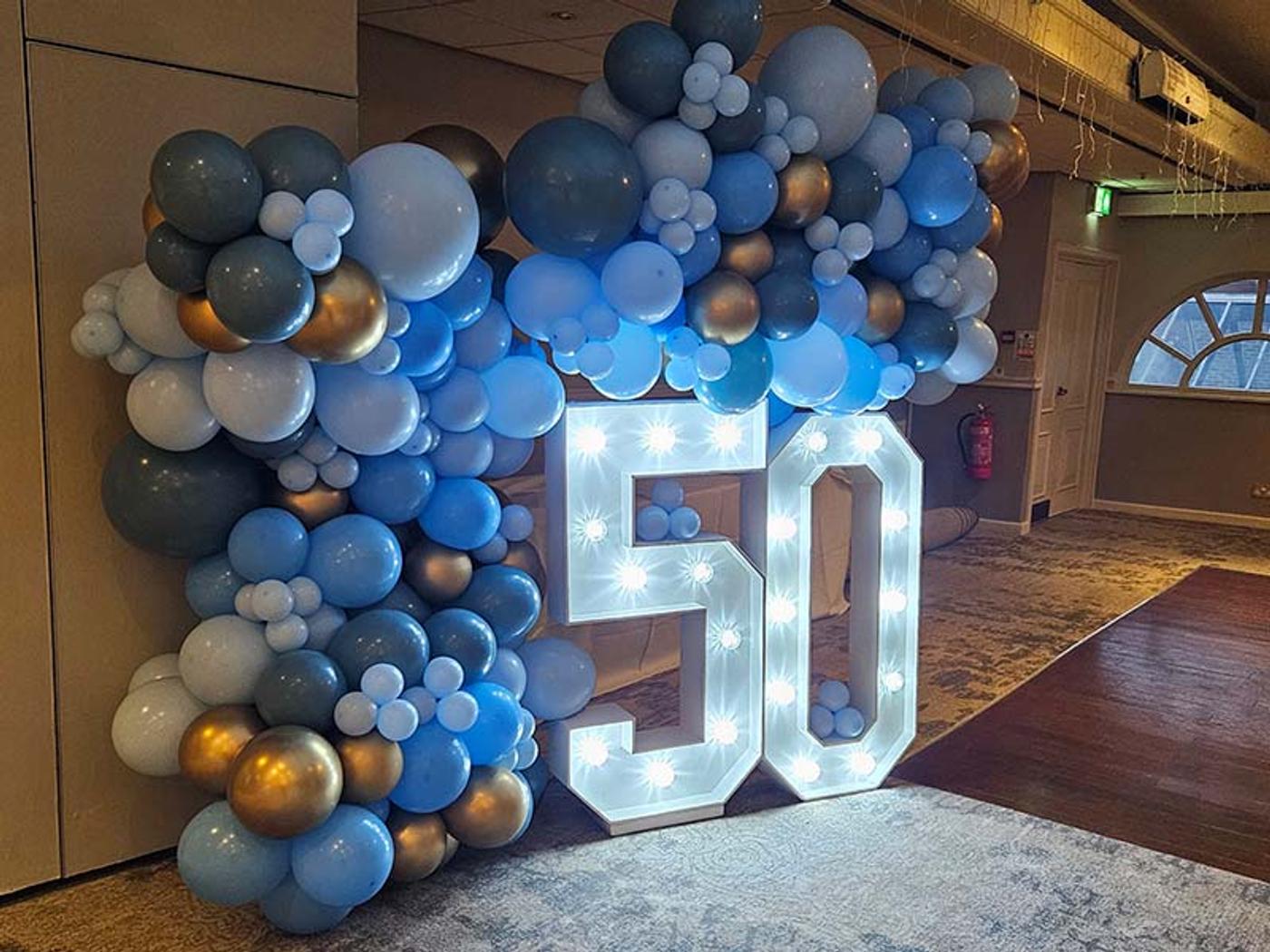 Blue, silver and gold balloon garland beside a light-up '50' display