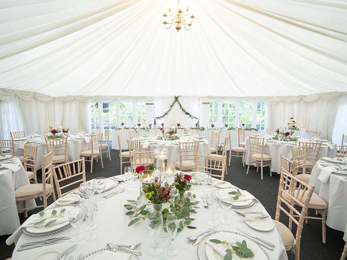 Marquee reception set with round tables and a floral arch backdrop