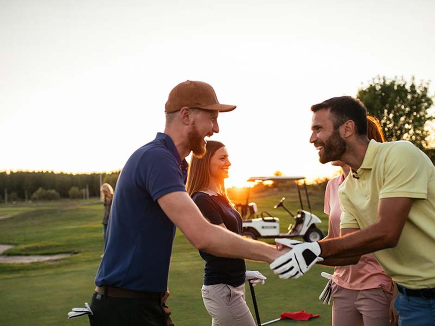 Golfer teeing off beside the lake with a golf buggy and guests at Delta Hotels Breadsall Priory Country Club