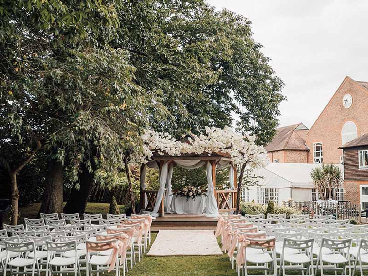 Gazebo ceremony set up with blush pink chair sashes beneath flowering trees