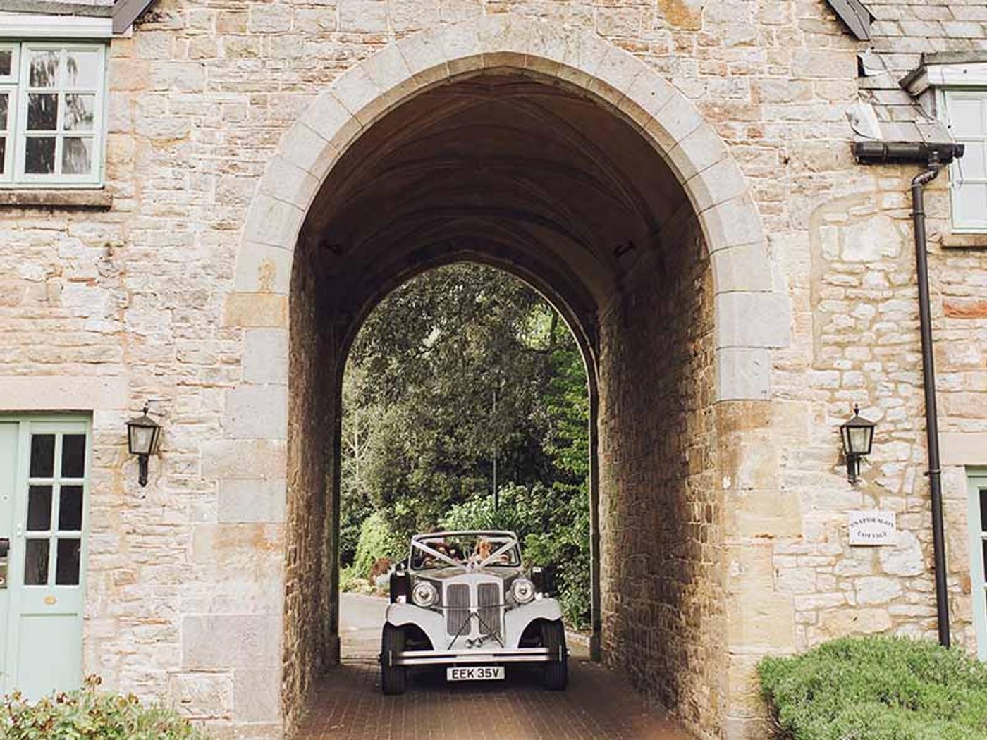 Vintage wedding car driving through the stone archway at Delta Hotels St. Pierre Country Club