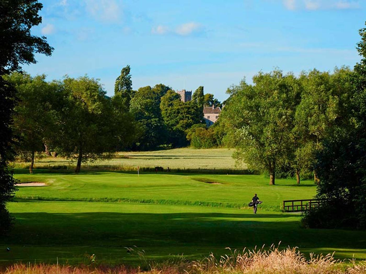 Golfer walking the fairway with Delta Hotels St. Pierre Country Club's manor house tower in the distance