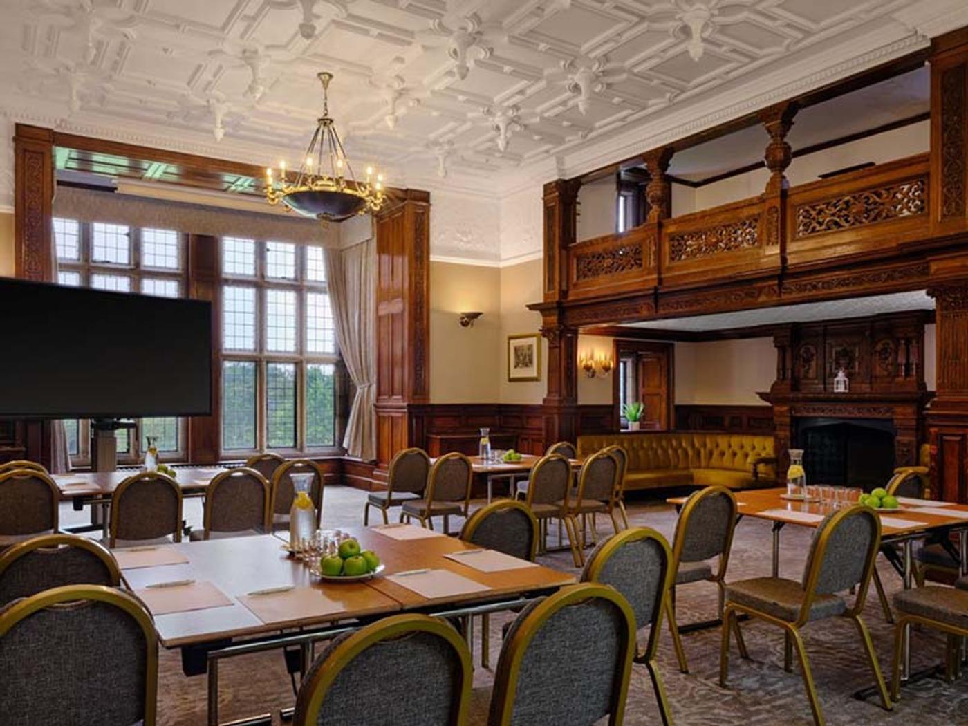 Oak-panelled hall set up for a conference with round tables and a projector screen