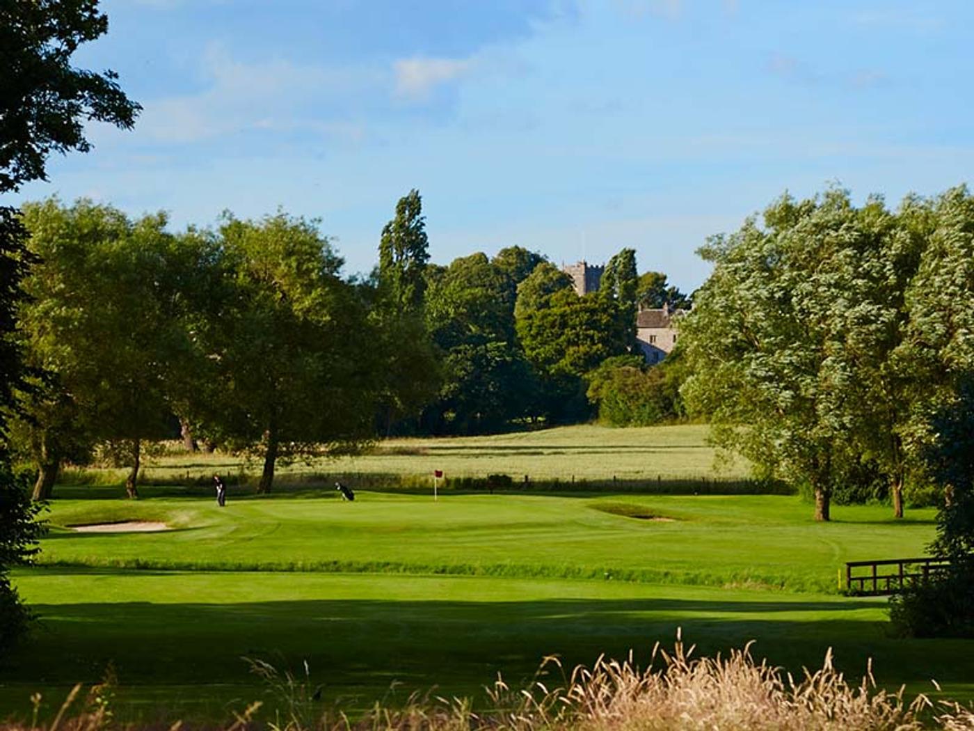 Golfers on the green with Delta Hotels St. Pierre Country Club's manor house tower visible beyond the trees