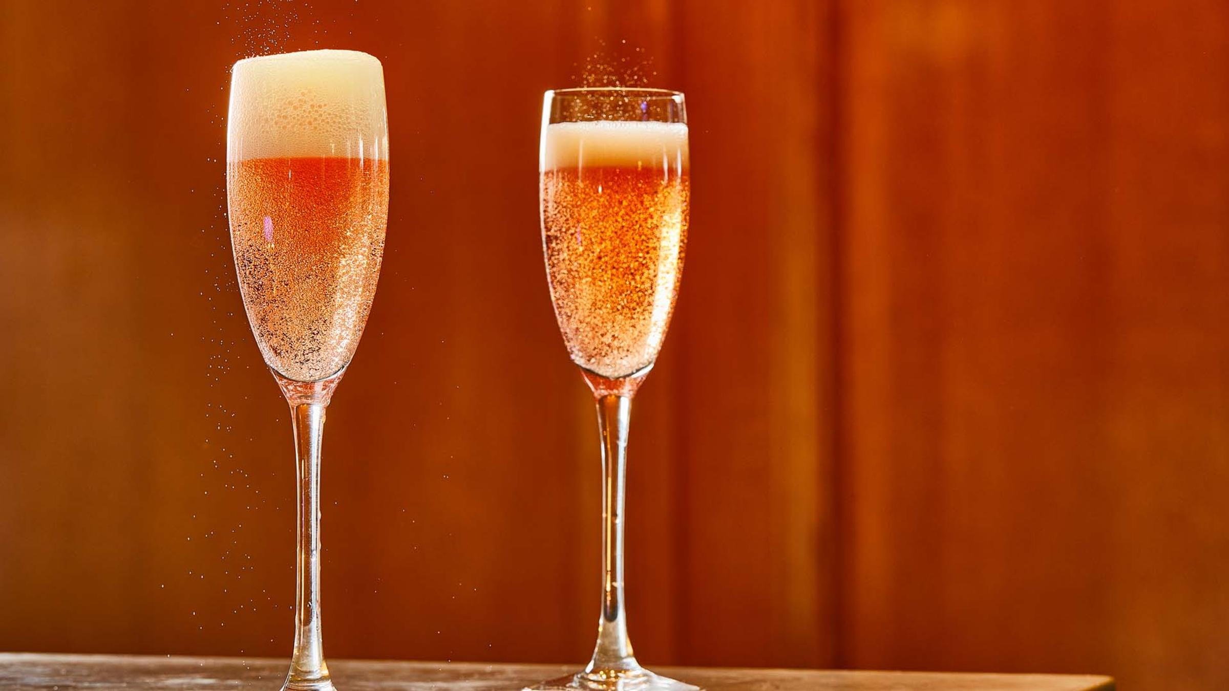 Two glasses of sparkling rosé wine against a warm copper backdrop