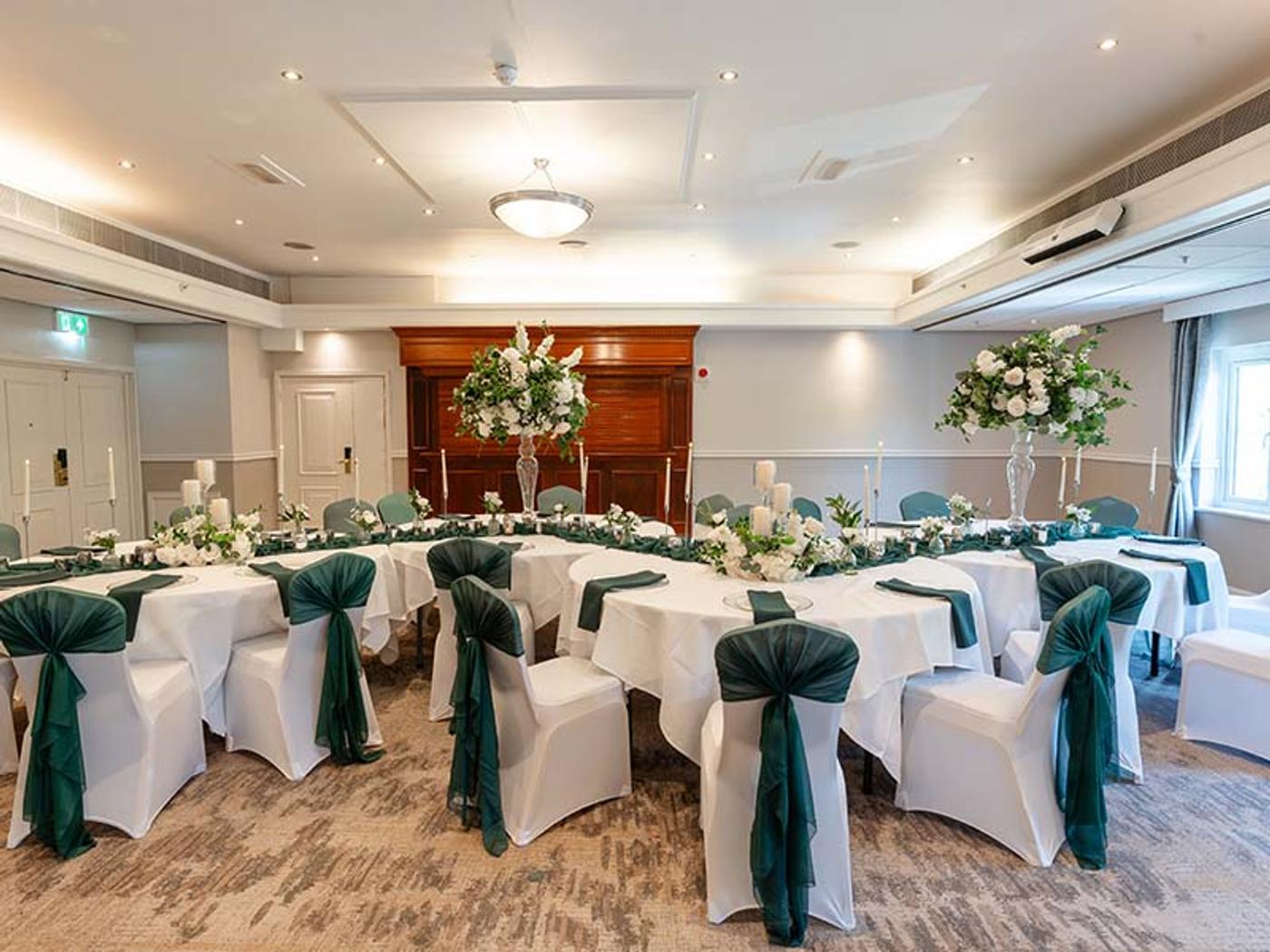 Thurnham Suite set banquet-style with green chair sashes and tall floral displays