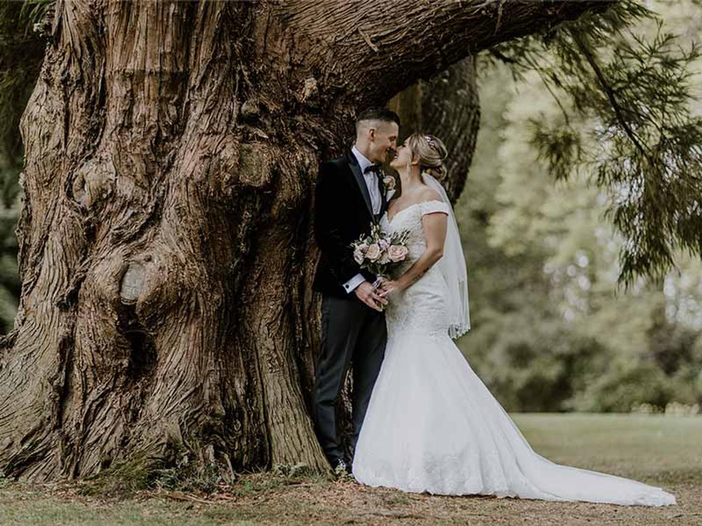 Bride and groom kissing beneath an ancient tree in Delta Hotels by Marriott Tudor Park Country Club's grounds
