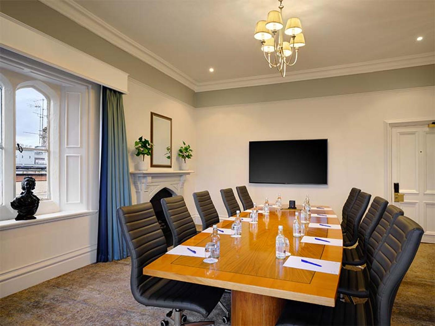 Period meeting room with a chandelier and a boardroom table by an arched window
