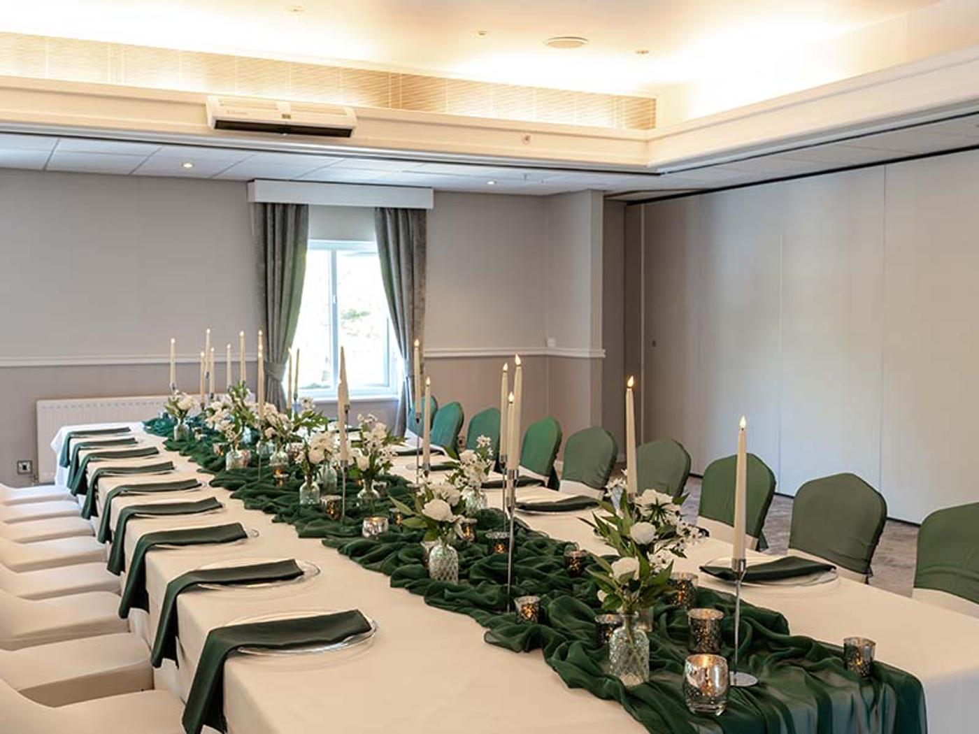 Long banquet table dressed with a green table runner and tall candlesticks in Thurnham Suite