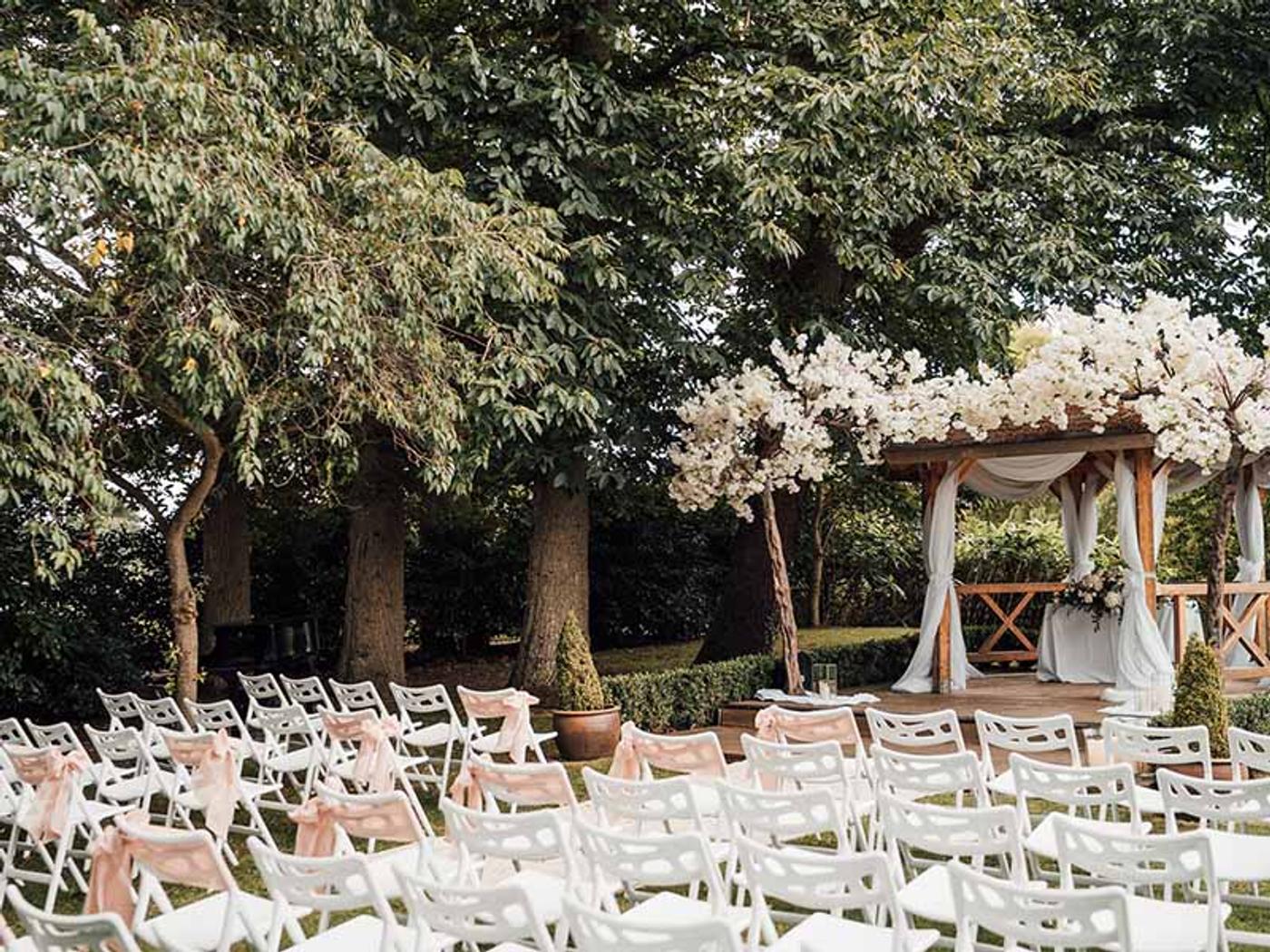 Guests' chairs with blush sashes lined up beneath the trees facing the gazebo