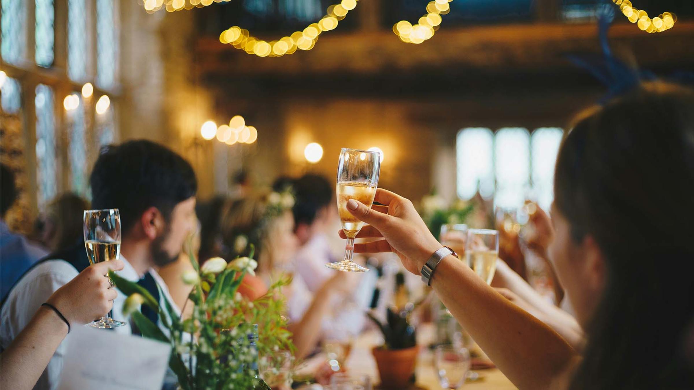 Guests raising champagne glasses in celebration, string lights glowing above