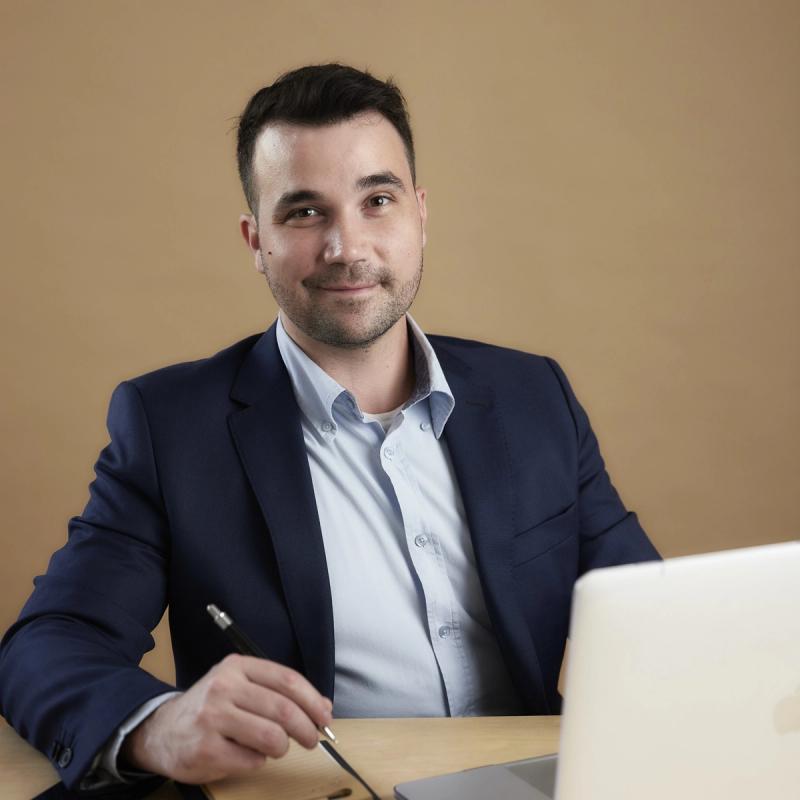O advogado sorrindo à mesa de trabalho, com caneta e notebook