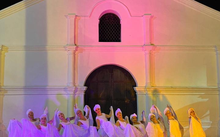 Bailarinas vestidas de blanco frente a una capilla iluminada de noche