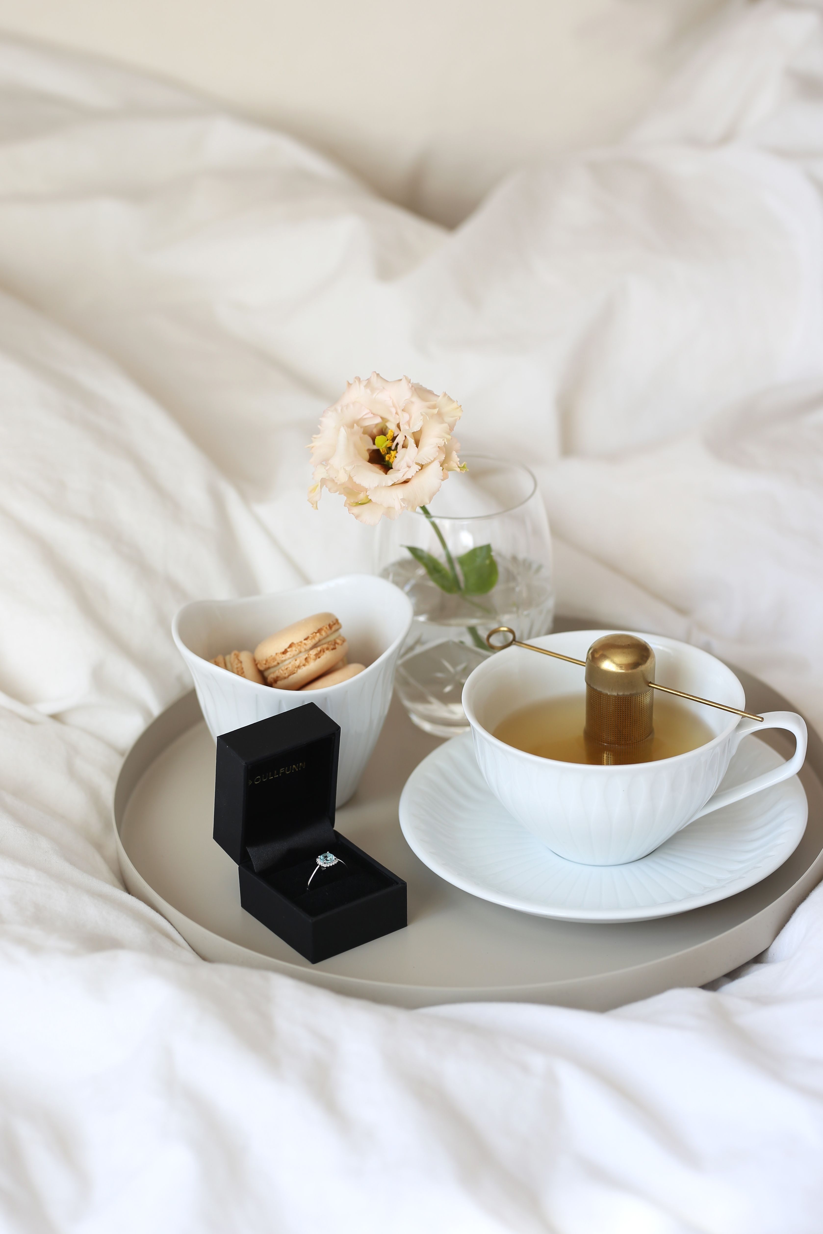 Tekopp, makroner, blomst og smykke på senga som morgengave etter bryllup