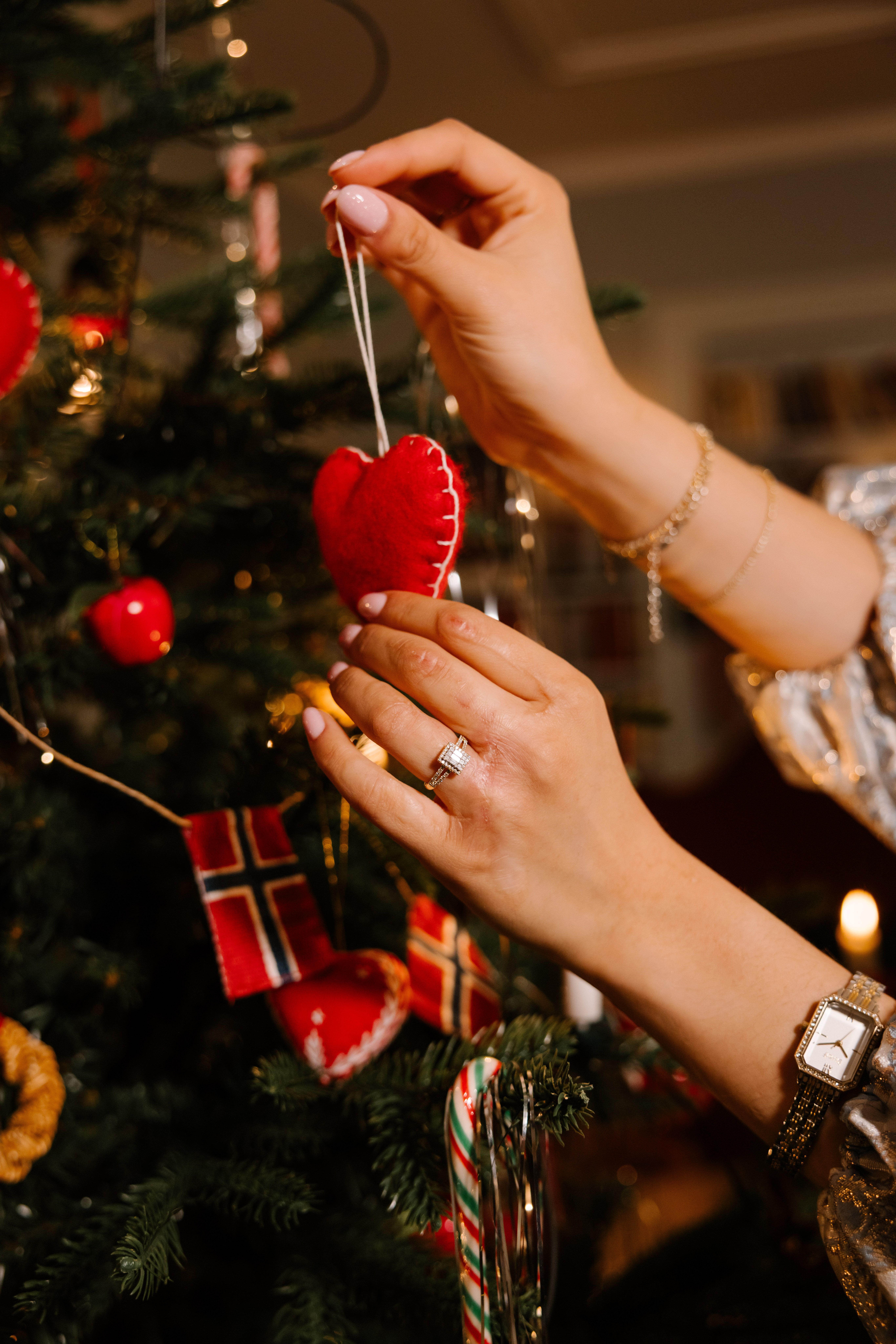 Hånd med en diamantring og en klokke som pynter et juletre
