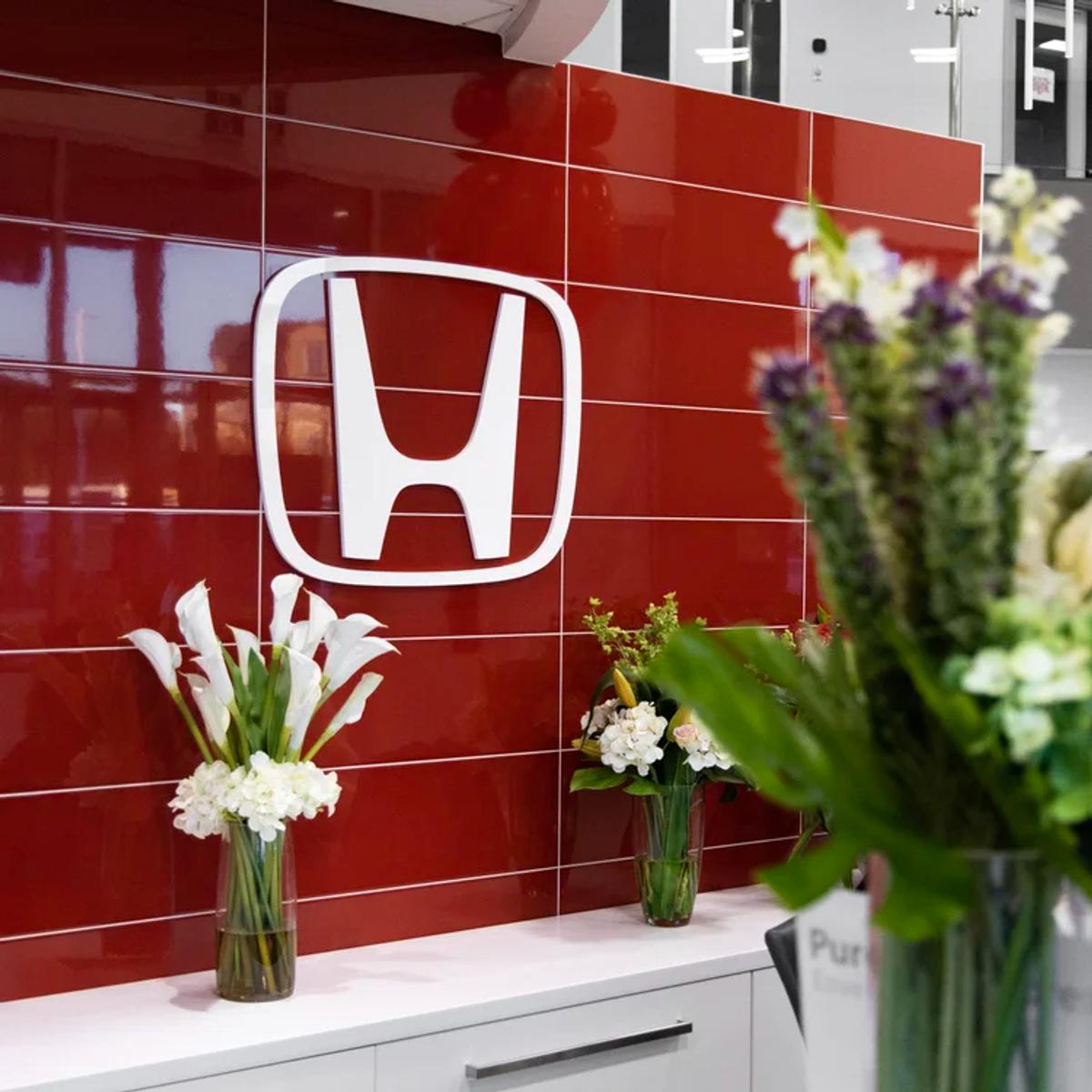 Honda logo mounted on a red tiled feature wall at Cambridge Honda, with floral arrangements on the counter.