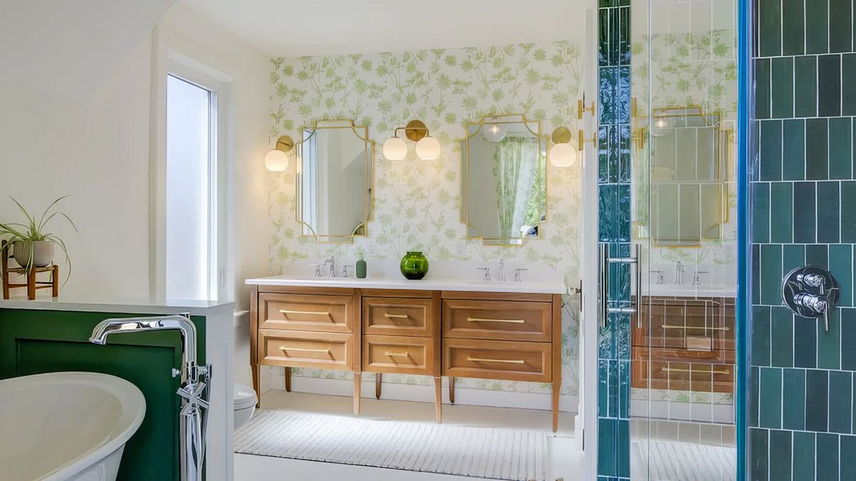 A finished ensuite with a wood double vanity, botanical wallpaper, brass-framed mirrors, and a glass shower, as seen in Jackman Ltd.’s Marc and Mandy segment.