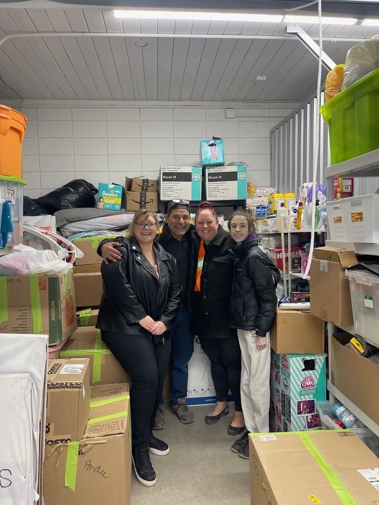 Jackman team members with Mamas for Mamas staff in a donation storeroom stacked with toys, food, and household supplies.