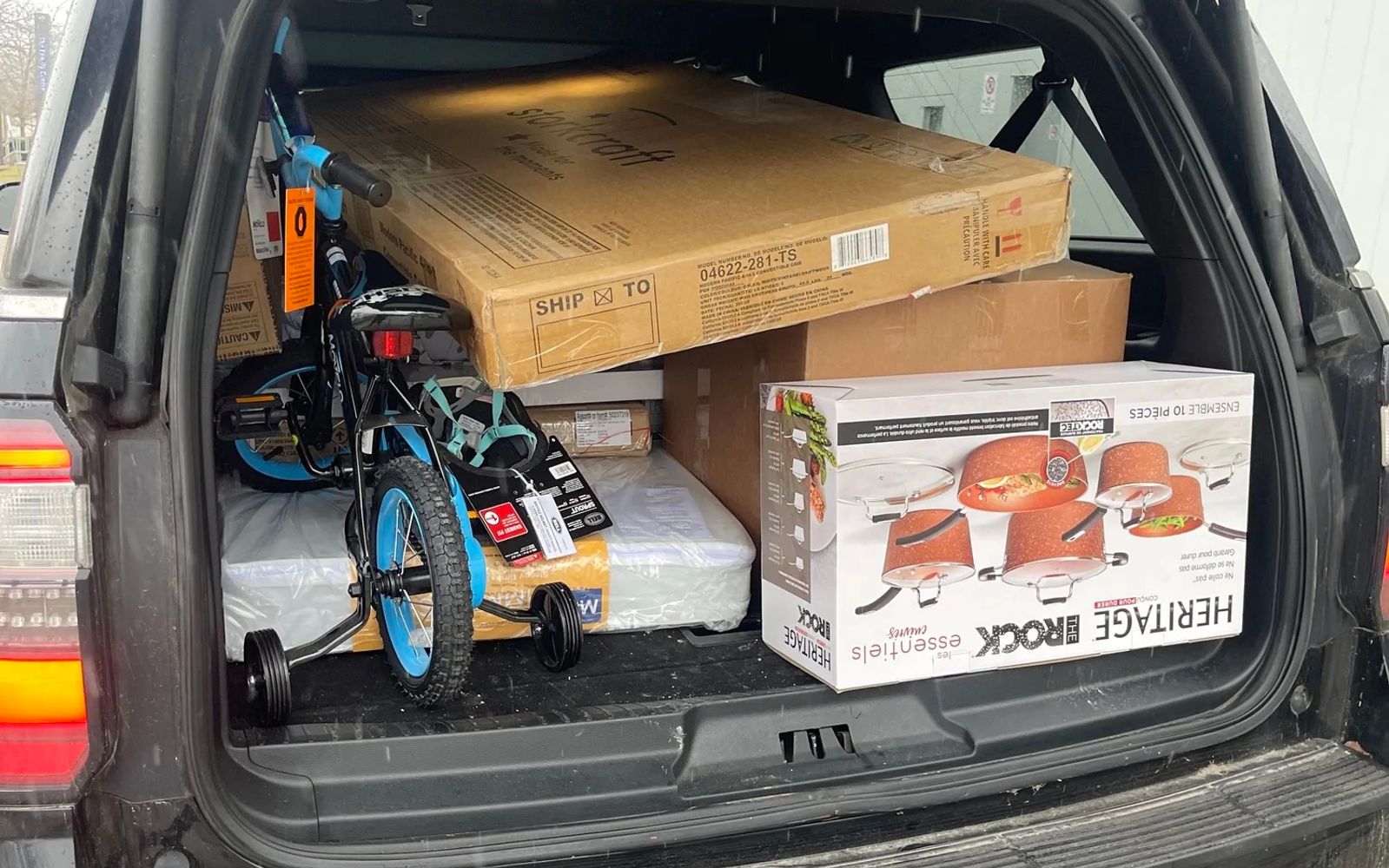 The open cargo area of an SUV packed with a child's bicycle, cookware, and boxed household donations.