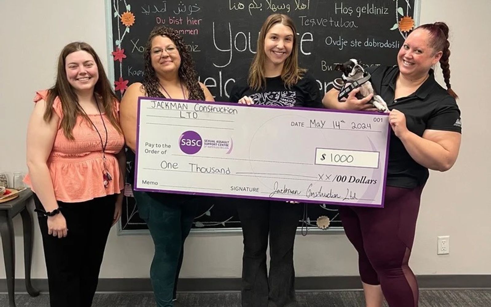 Jackman Construction and SASCWR staff holding a $1,000 ceremonial cheque, with therapy dog Ellie.