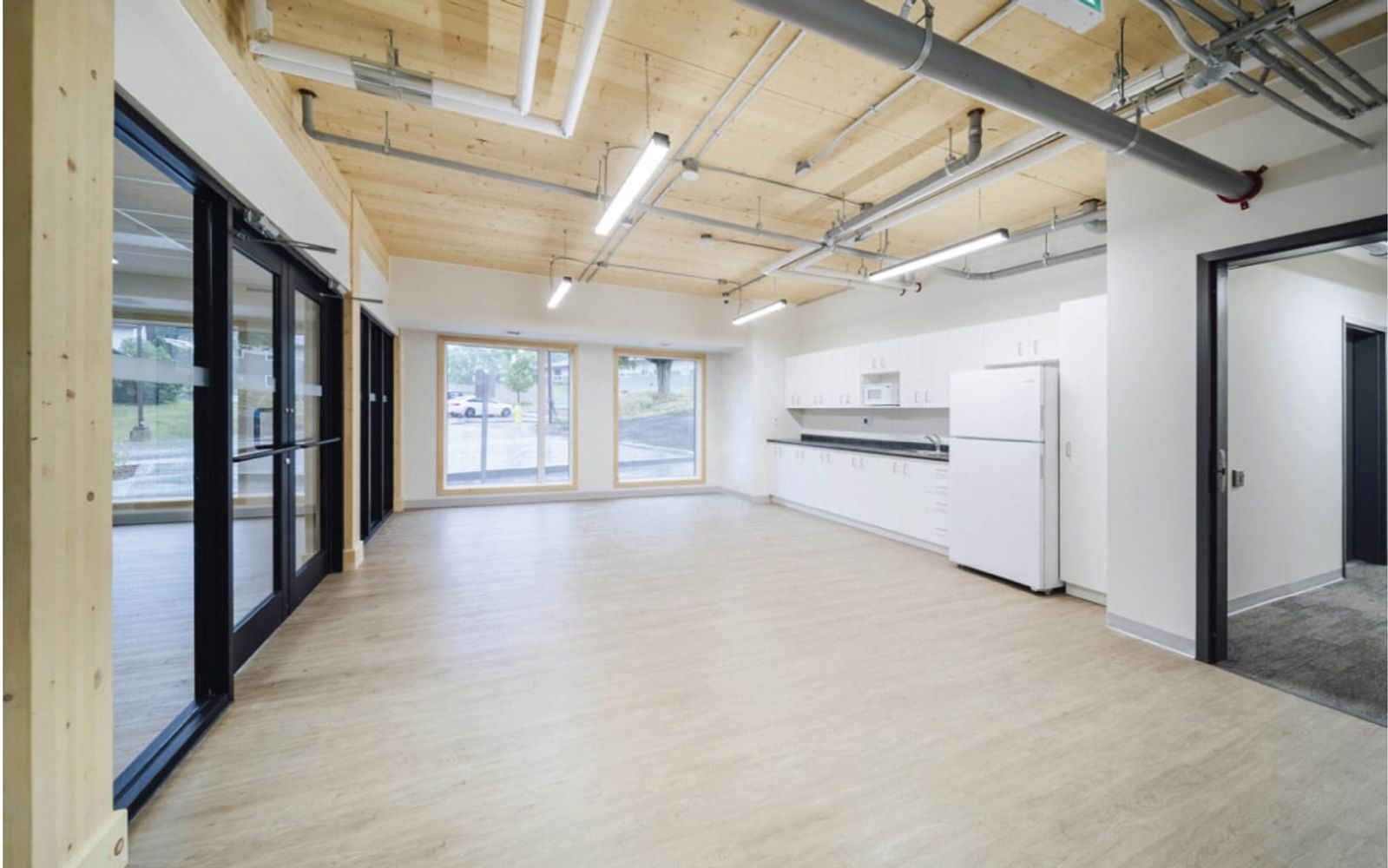 Common kitchen and lounge at Passage House with an exposed mass timber ceiling and glass doors to the exterior.