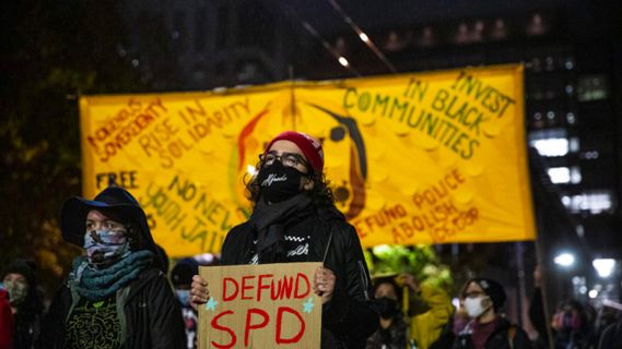 A demonstrator holds a mask that reads Defund SPD