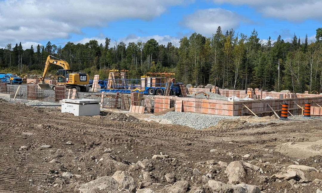 The foundation of an under-construction modular home factory, with a construction CAT and other materials and vehicles in it