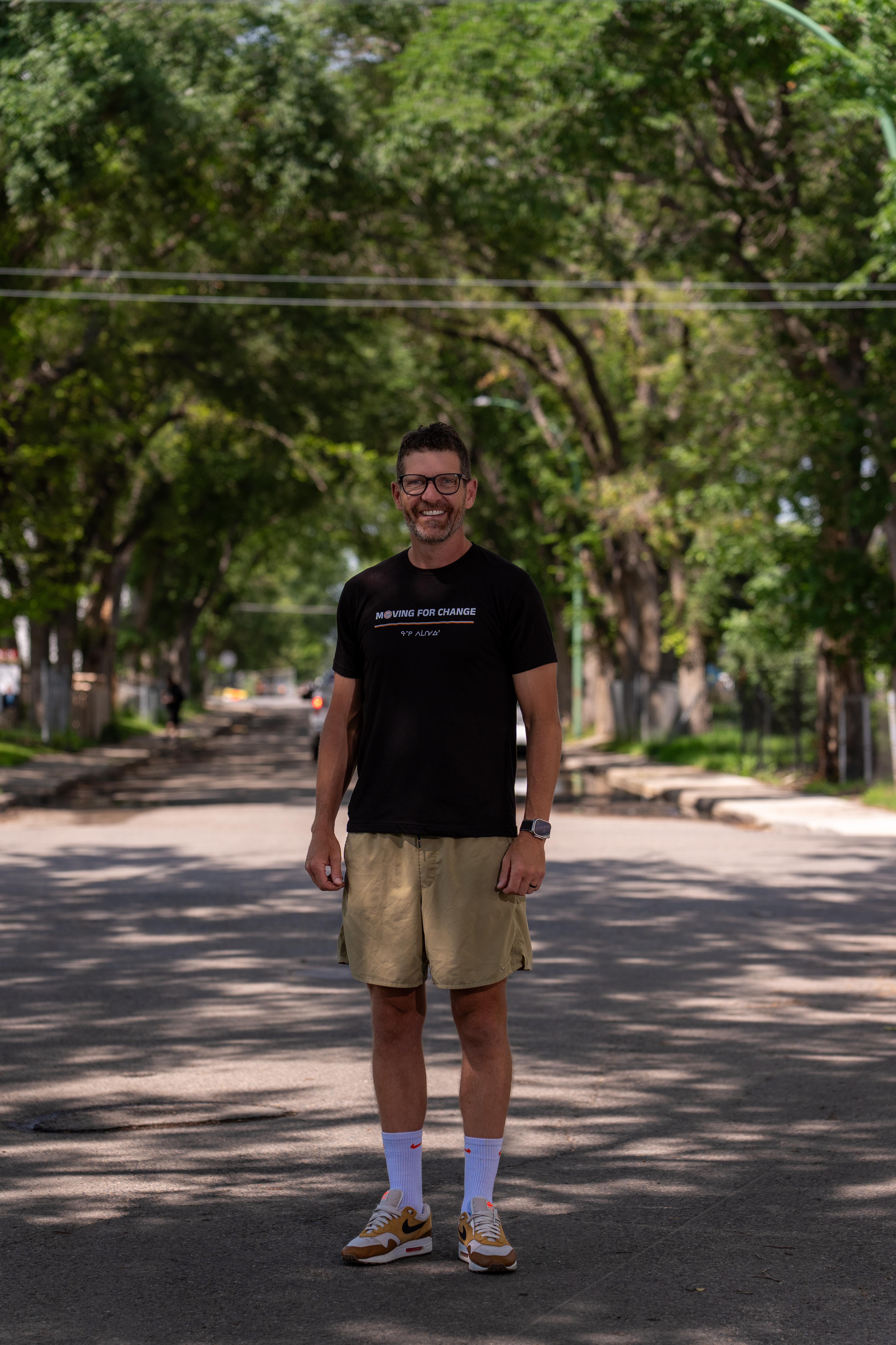 Brian Lewis stands in a street wearing a t-shirt that says "Moving For Change."