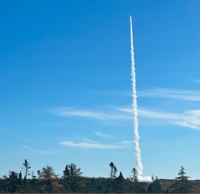 A wide view of a rocket launching at Spaceport Nova Scotia against a deep blue sky