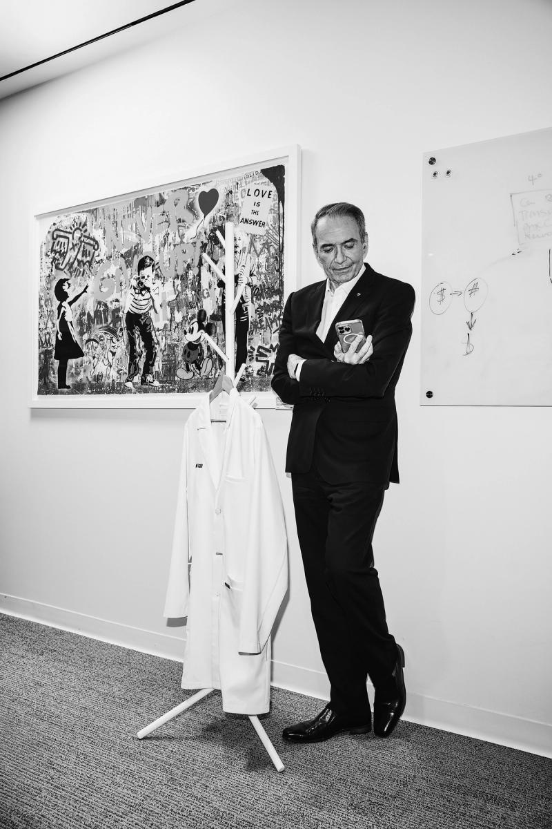 Kevin Smith stands next to a white lab coat on a hanger, looking at an iPhone