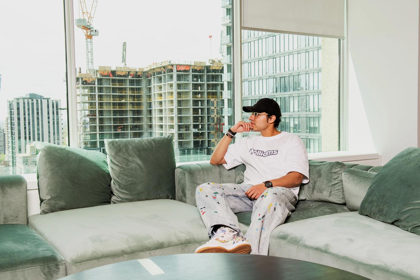 Swish Goswami sits on a couch looking out a window where under-construction building is visible