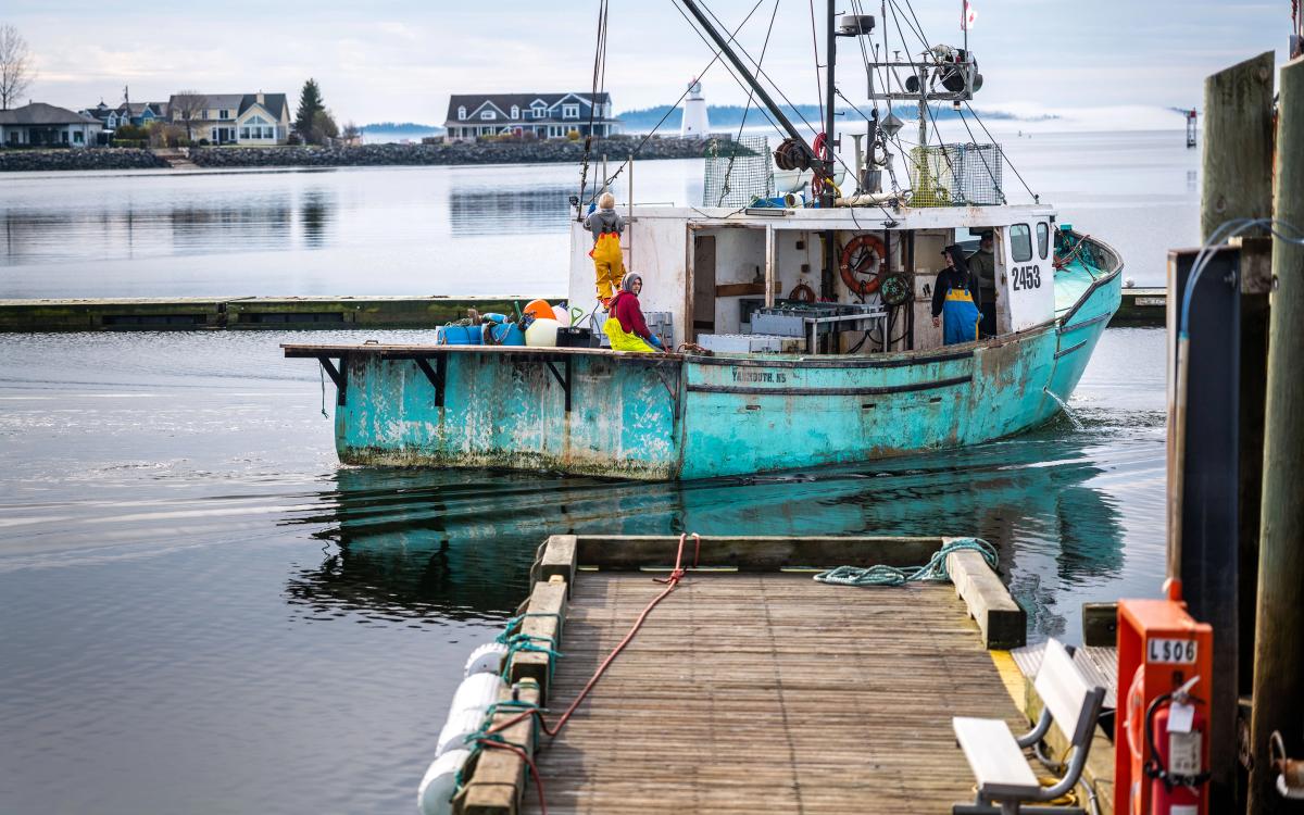 A turquoise blue lobster and crab fishing vessel with the name All Done and a crew of fishers working on it pulls out of the wharf filled with ropeless fishing gear near St. Andrews New Brunswick